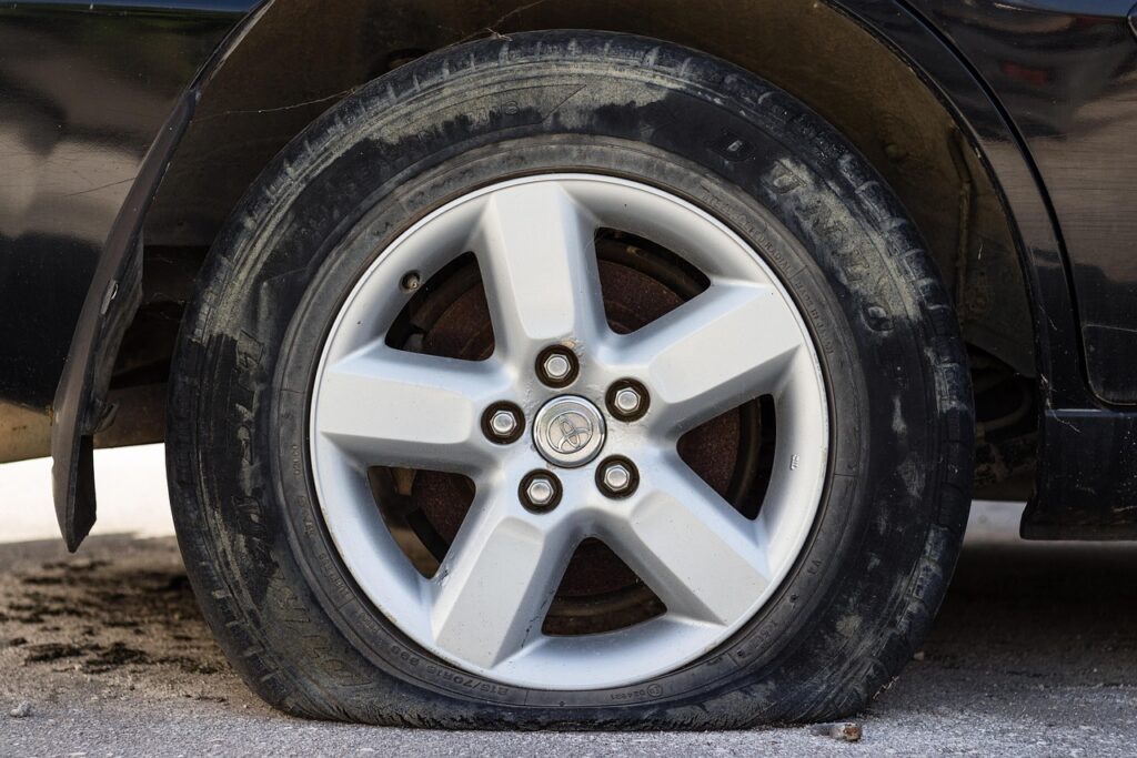 Close-up of a deflated car tyre sagging against a UK road surface, showing worn tread and low air pressure, illustrating tyre safety risks.