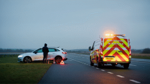 UK roadside breakdown scene with a modern car stopped on the hard shoulder, hazard lights on, and a warning triangle placed behind the vehicle. A Reds Recovery Service van is parked nearby under overcast skies, showing professional roadside assistance in Kent.
