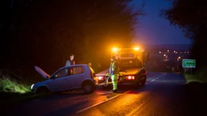 Recovery truck assisting a broken-down car at night in Sevenoaks, with the driver speaking to an operator under amber lights for safe 24-hour roadside help.